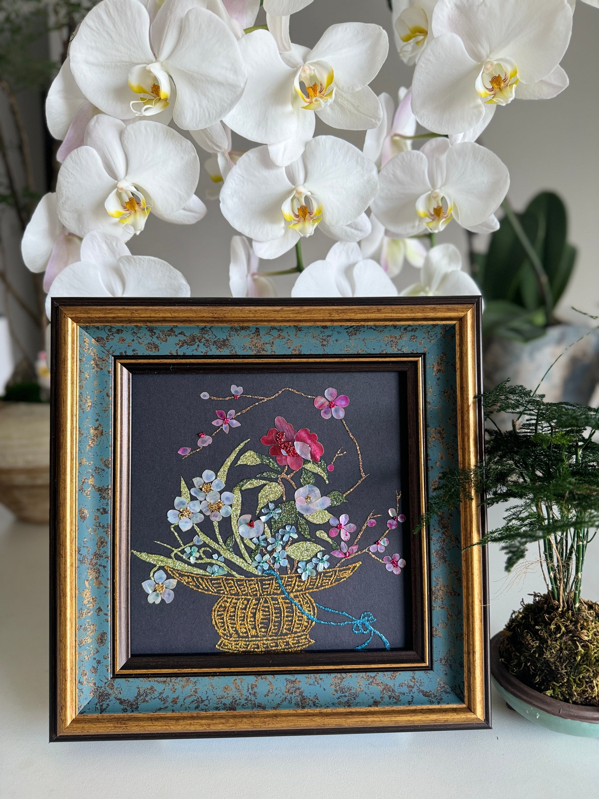Luxury Zen home decor presentation featuring the "Three Friends of Winter" oriental shell artwork displayed next to a minimalist green kokedama bonsai plant.