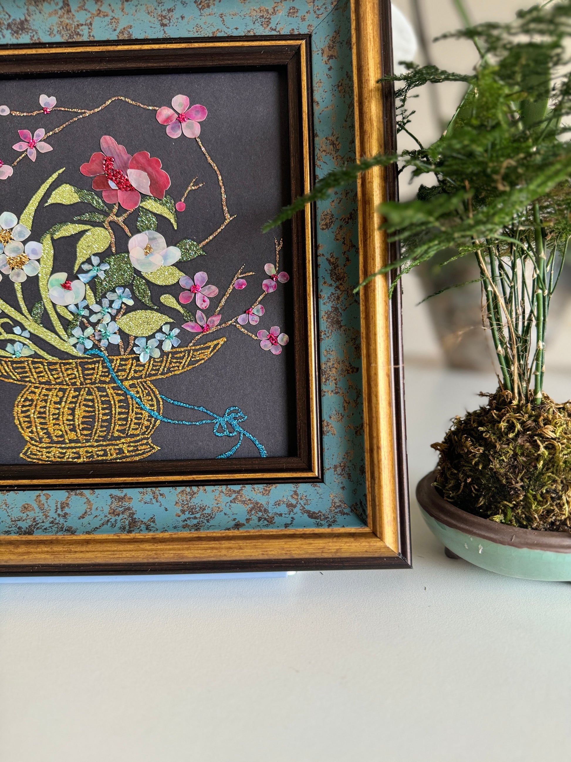 Luxury Zen home decor presentation featuring the "Three Friends of Winter" oriental shell artwork displayed next to a minimalist green kokedama bonsai plant.