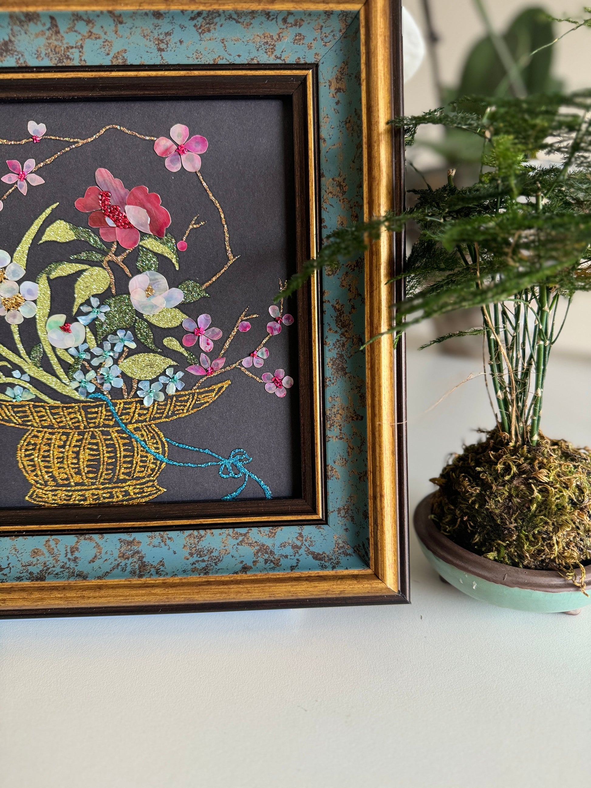 Luxury Zen home decor presentation featuring the "Three Friends of Winter" oriental shell artwork displayed next to a minimalist green kokedama bonsai plant.