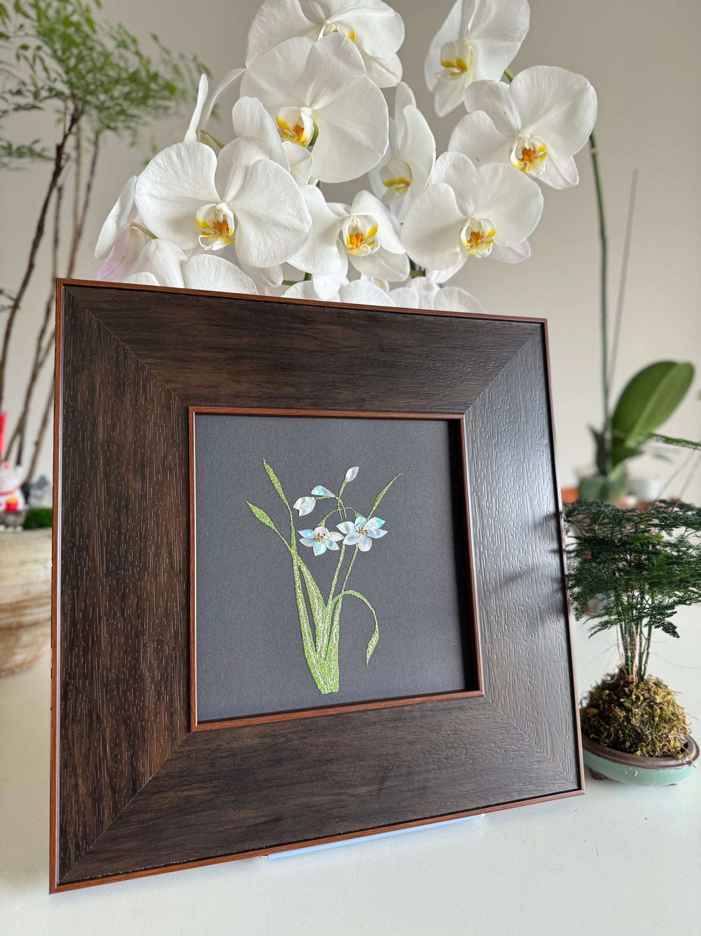 Handcrafted mother-of-pearl inlay artwork "Luo Shen Fu" featuring minimal, elegant narcissus water daffodil flowers on a matte black canvas, housed in a luxurious wide dark wood frame.
