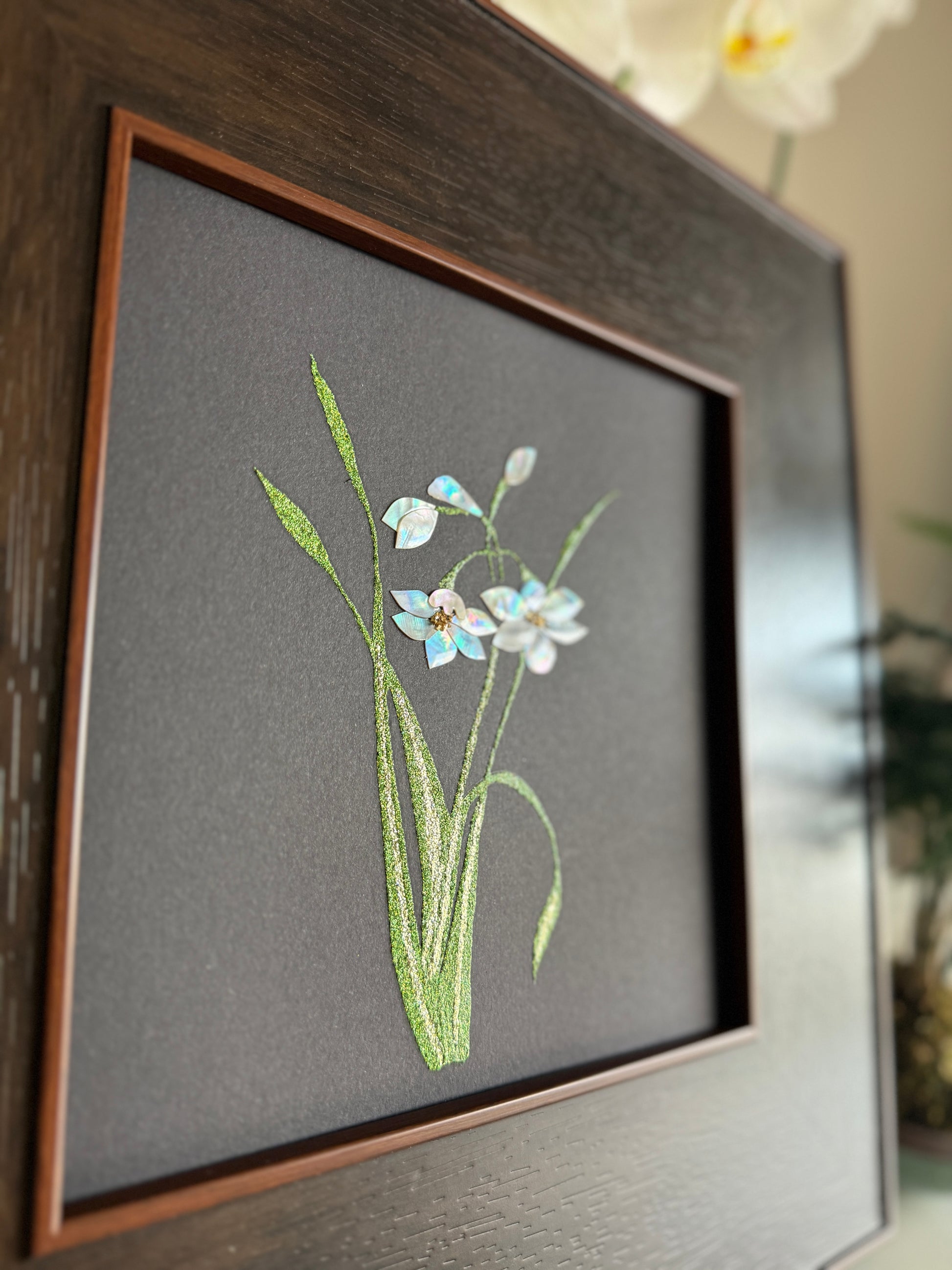 Macro photographic view of traditional Raden technique highlighting the crystalline white and soft blue iridescence of hand-cut natural shell petals and fine glittery green leaves.
