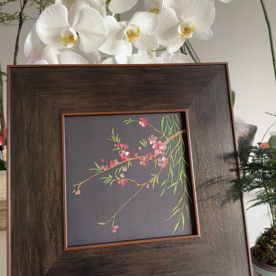 Premium boutique botanical home decor presentation featuring the handcrafted "Smile of Spring" peach blossom shell mosaic painting displayed against a backdrop of elegant white orchids.
