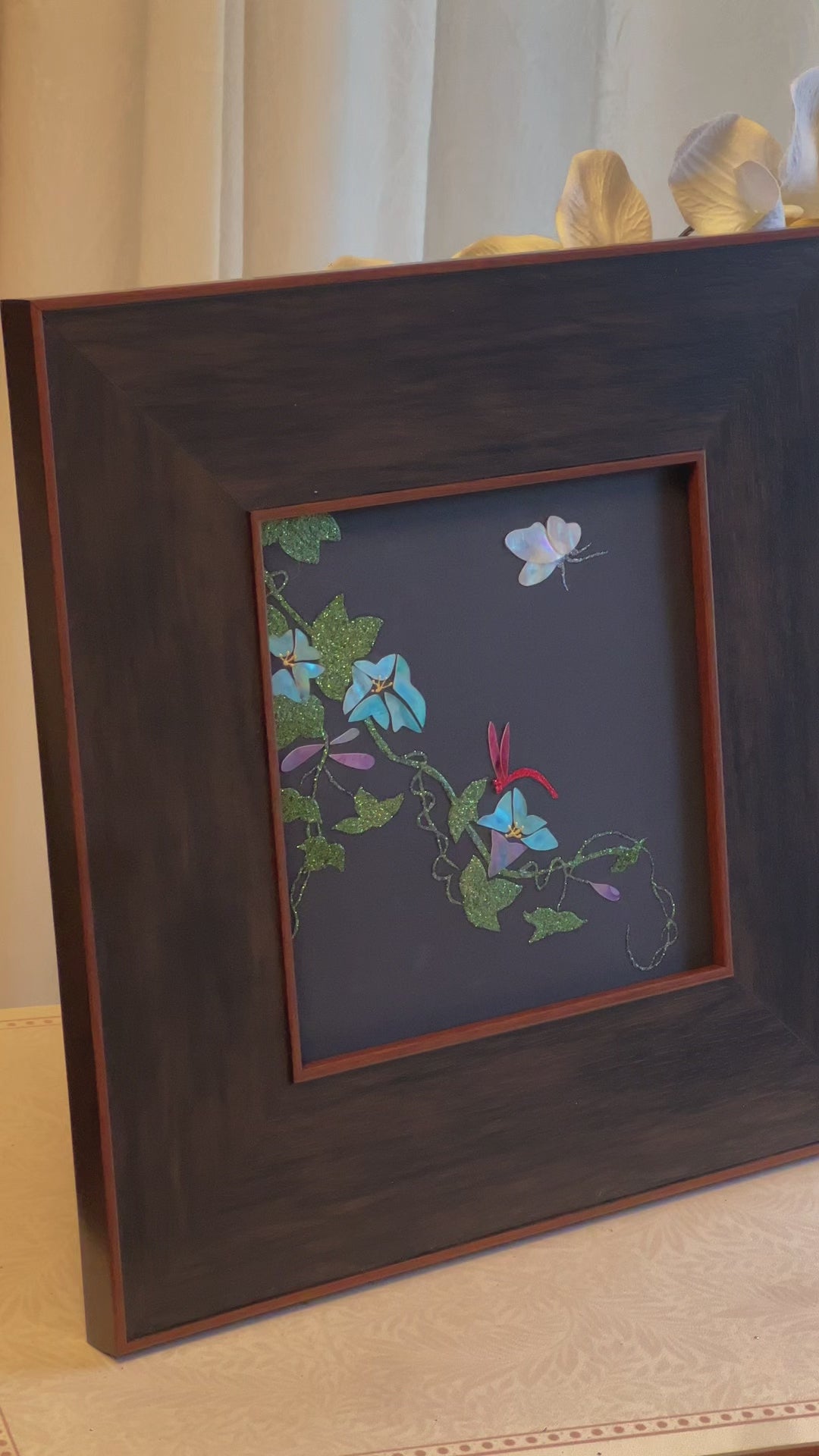 Original Raden shell art titled The Morning Glory by Showing Studio in a 35x35cm wide margin dark walnut frame, showcasing icy blue mother of pearl blossoms, a white shell butterfly, and a crimson dragonfly
